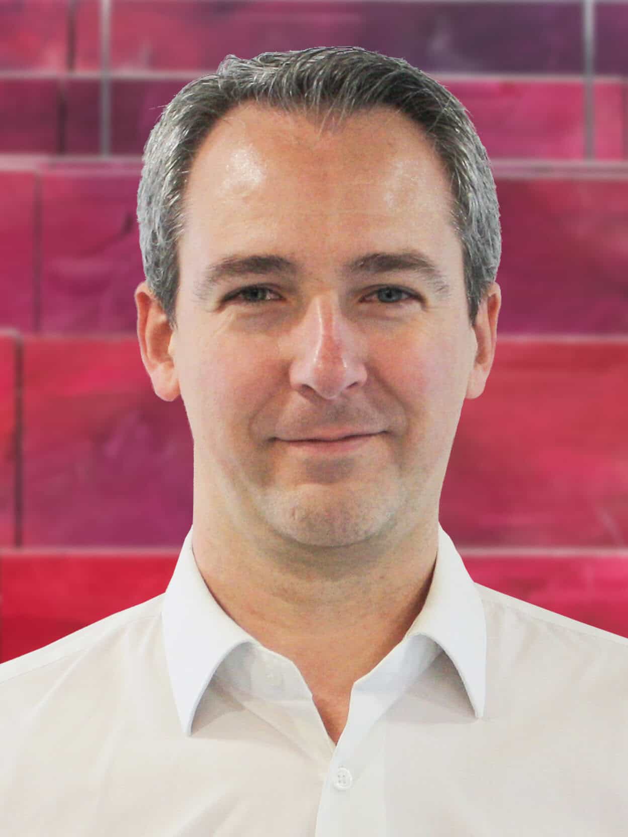 Homme professionnel souriant devant un fond rouge, représentant l'expertise de UBY dans le secteur.