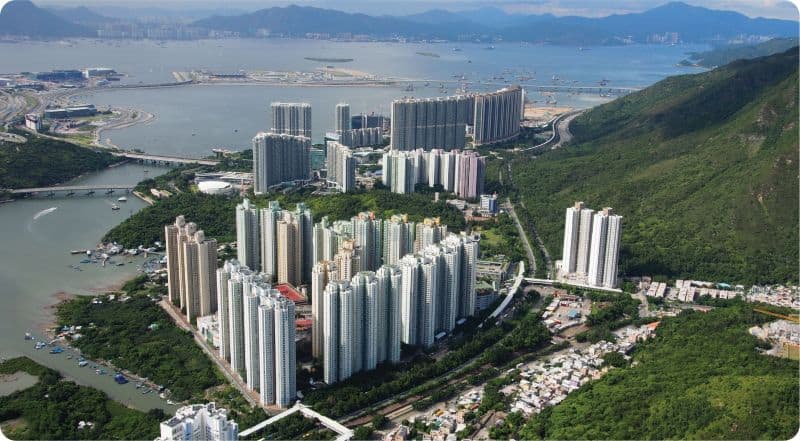 Haut de page, vue aérienne de Tung Chung à Hong Kong avec bâtiments modernes et montagnes environnan.