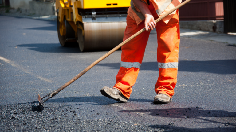 Man at a construction site smoothing out an asphalt surface for industrial monitoring